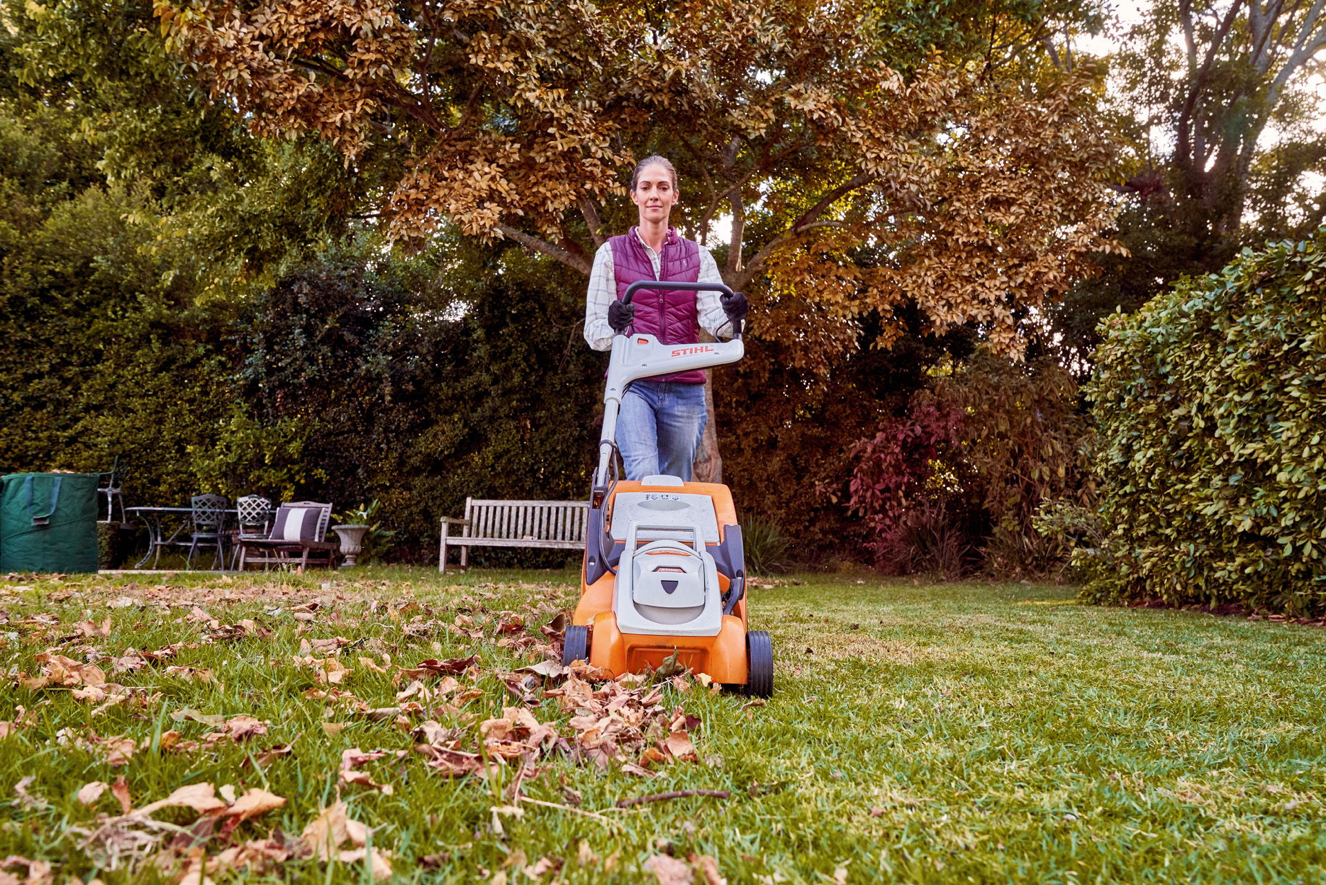Egy nő STIHL RMA 339 C akkumulátoros fűnyíróval őszi gyepápolást végez egy kertben