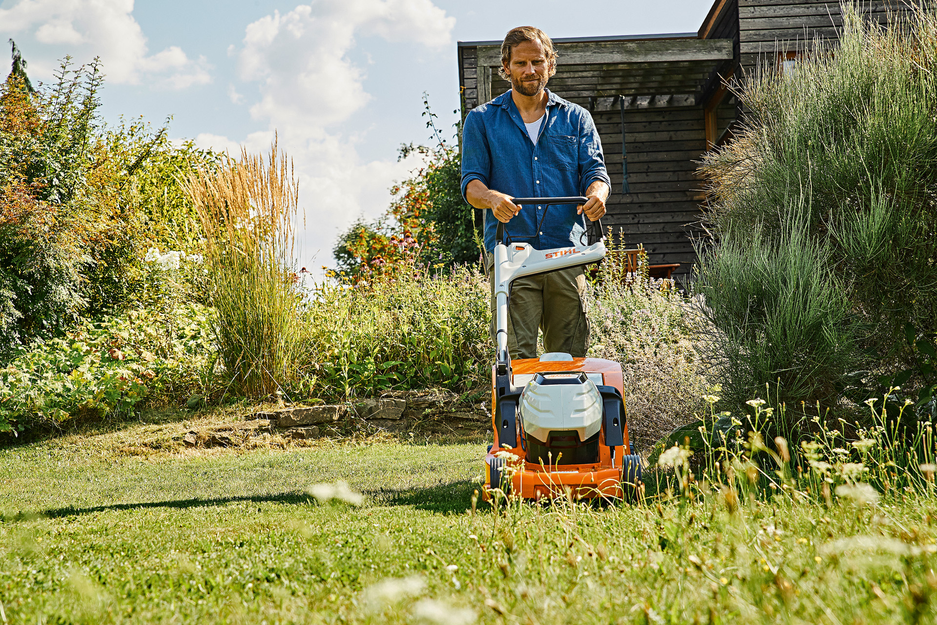 Egy férfi STIHL RMA 448 P-C akkumulátoros fűnyíróval gyepet ápol nyáron egy növényekkel borított területen