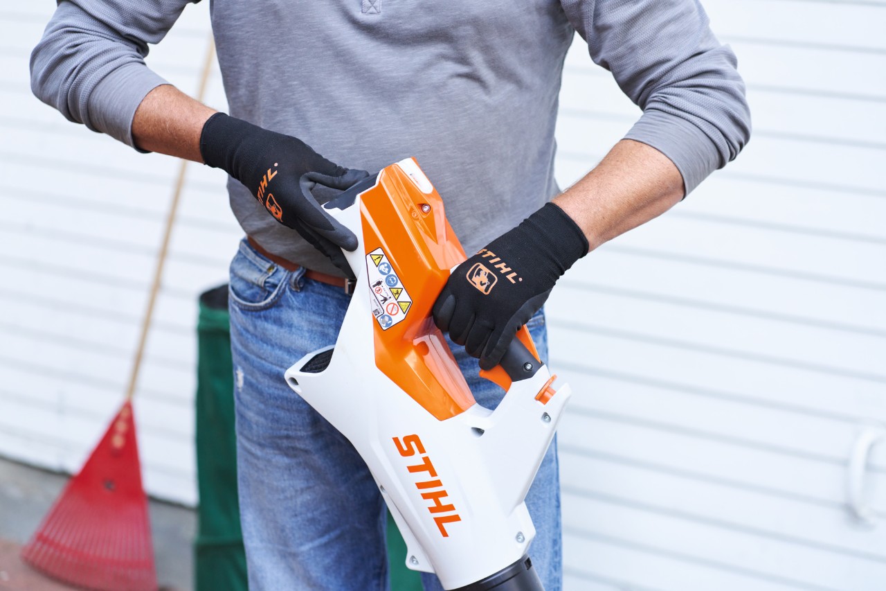 Egy ember szürke pulóverben és farmerben kezében STIHL lombfúvót tart