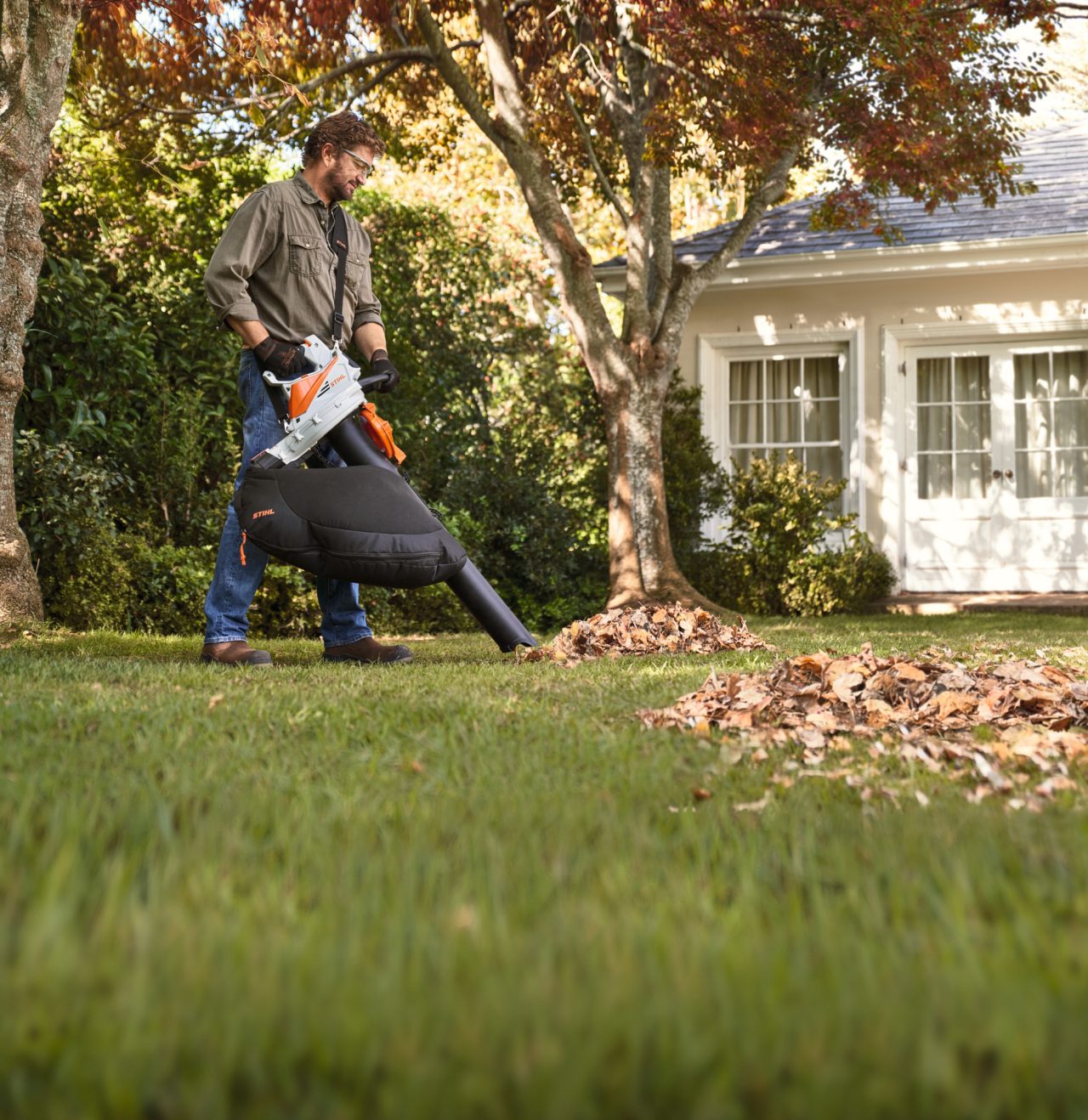 Egy STIHL SH 56 lomszívó szecskázógéppel egy ember felszívja a faleveleket a kertben, hogy kidobja őket 