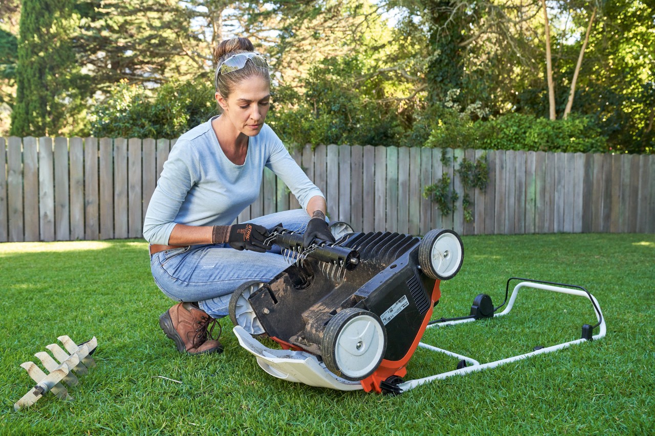 Védőszemüveget és munkakesztyűt viselő nő kicseréli a STIHL RLA 240 akkumulátoros gyepszellőztető lazítóegységét