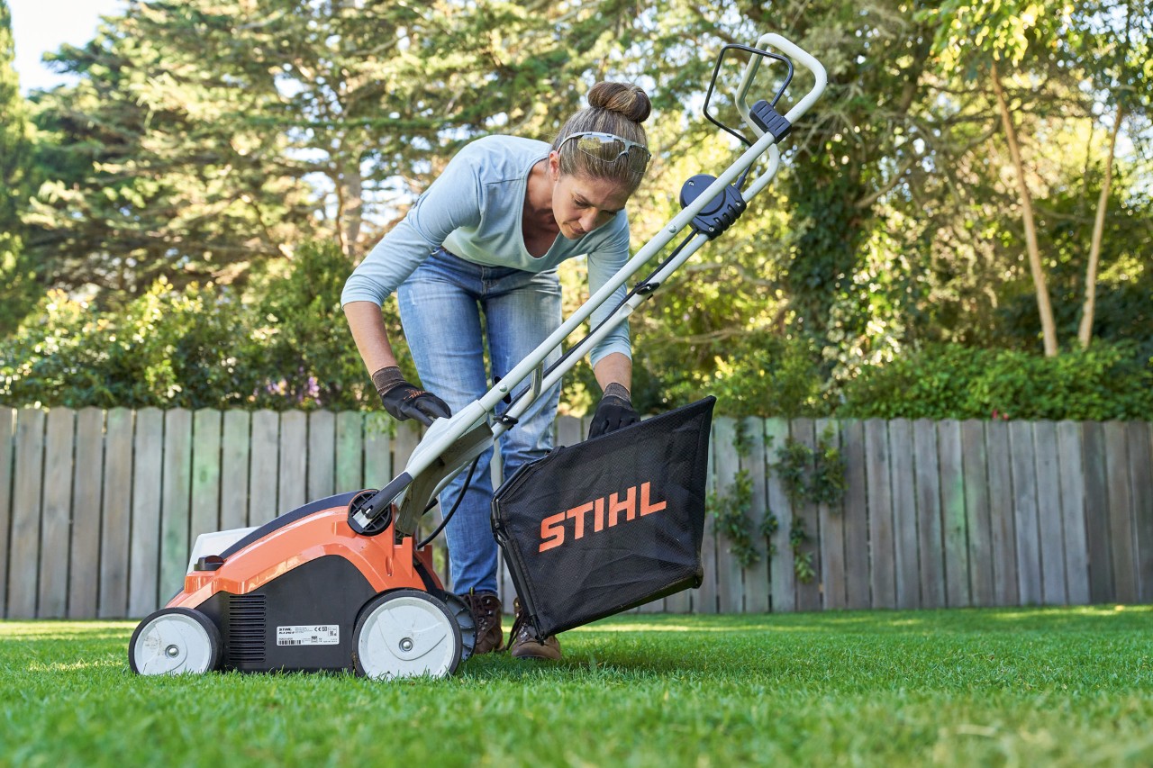 Egy nő felakasztja a STIHL RLA 240 akkumulátoros gyepszellőztető gyűjtőkosarát a készülék hátuljára.