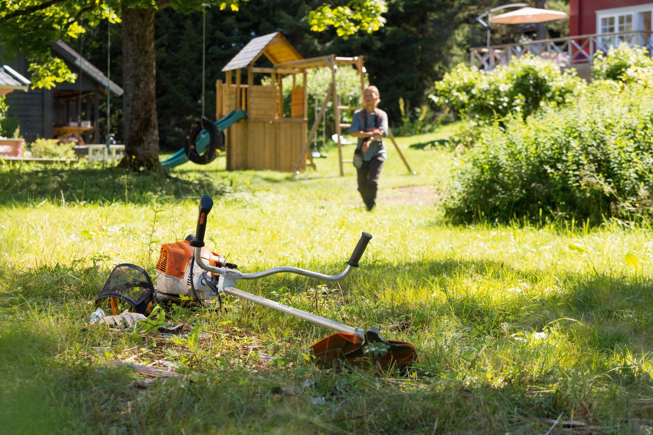 Egy STIHL FS 240 motoros kasza a fűben, a háttérben egy férfi készül a karbantartásra