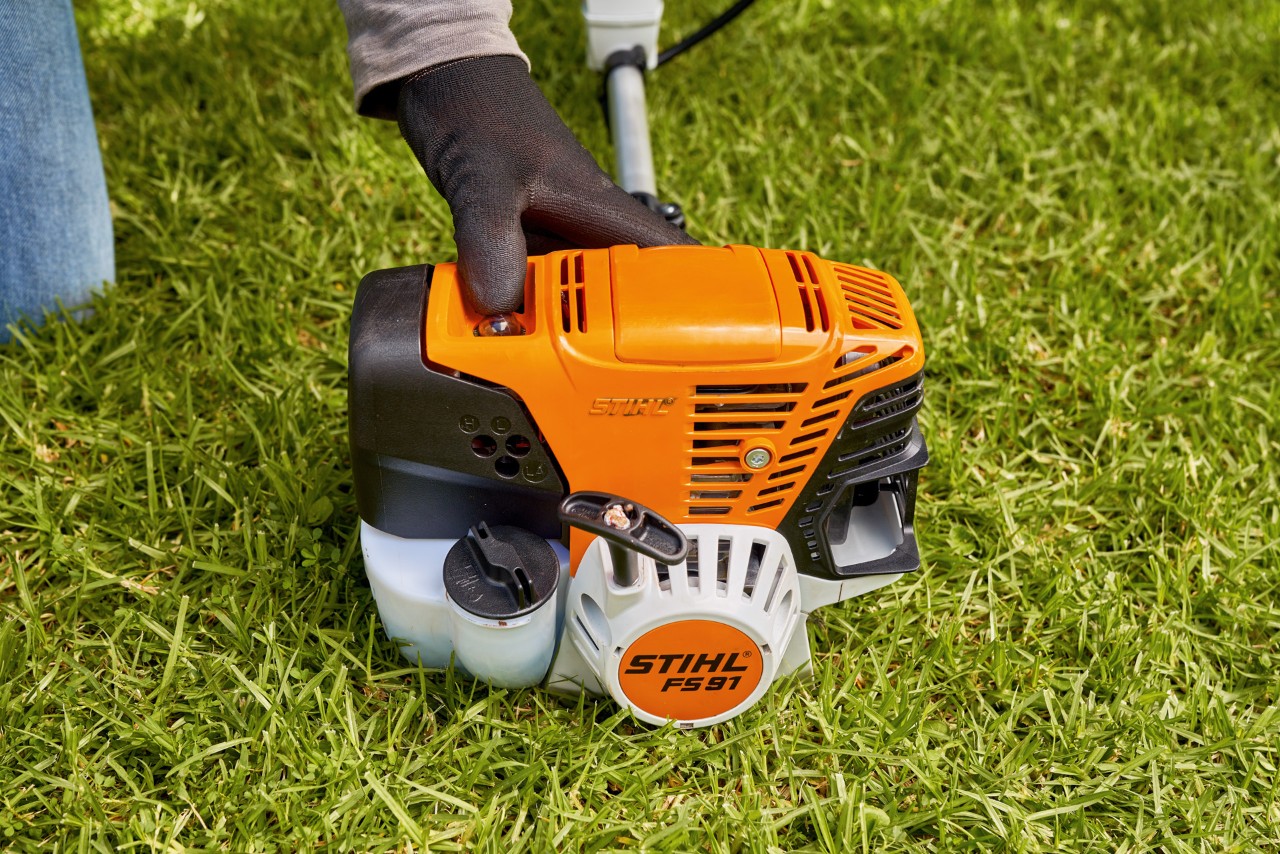 Egy férfi megnyomja a STIHL FS 91 benzinmotoros kasza üzemanyag-szivattyúját a beindításhoz