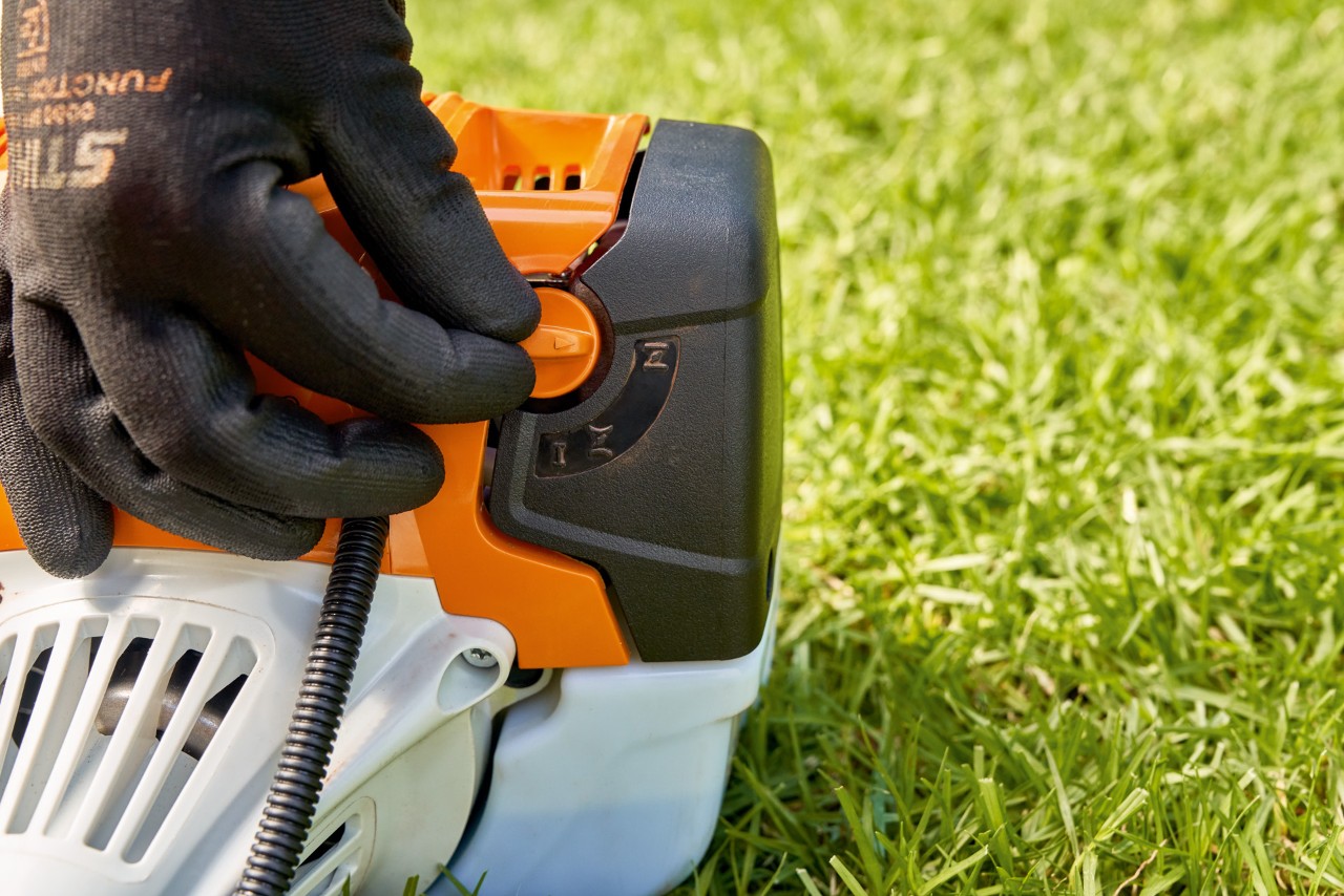 Egy férfi beállítja a STIHL FS 91 benzinmotoros kasza üzemanyag-szivattyújának karját a beindításhoz