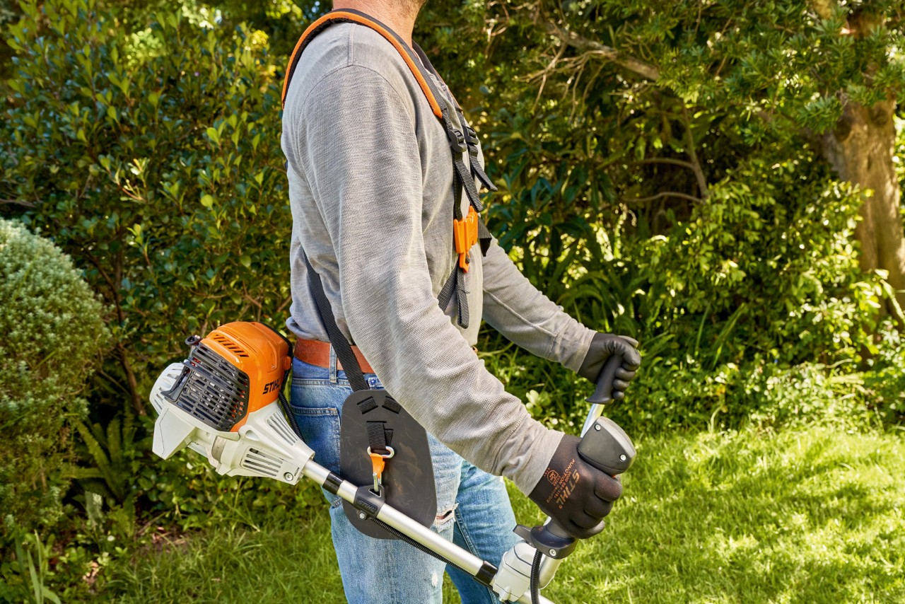 Egy férfi felemeli a STIHL FS 91 benzinmotoros kaszát a földről, hogy megkezdje a nyírást 