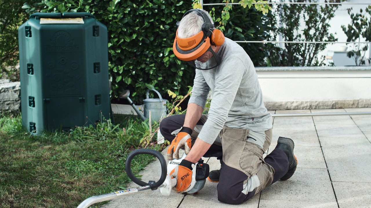 A STIHL FS 38 benzinmotoros kaszát egy védőruhát viselő férfi a földhöz nyomja