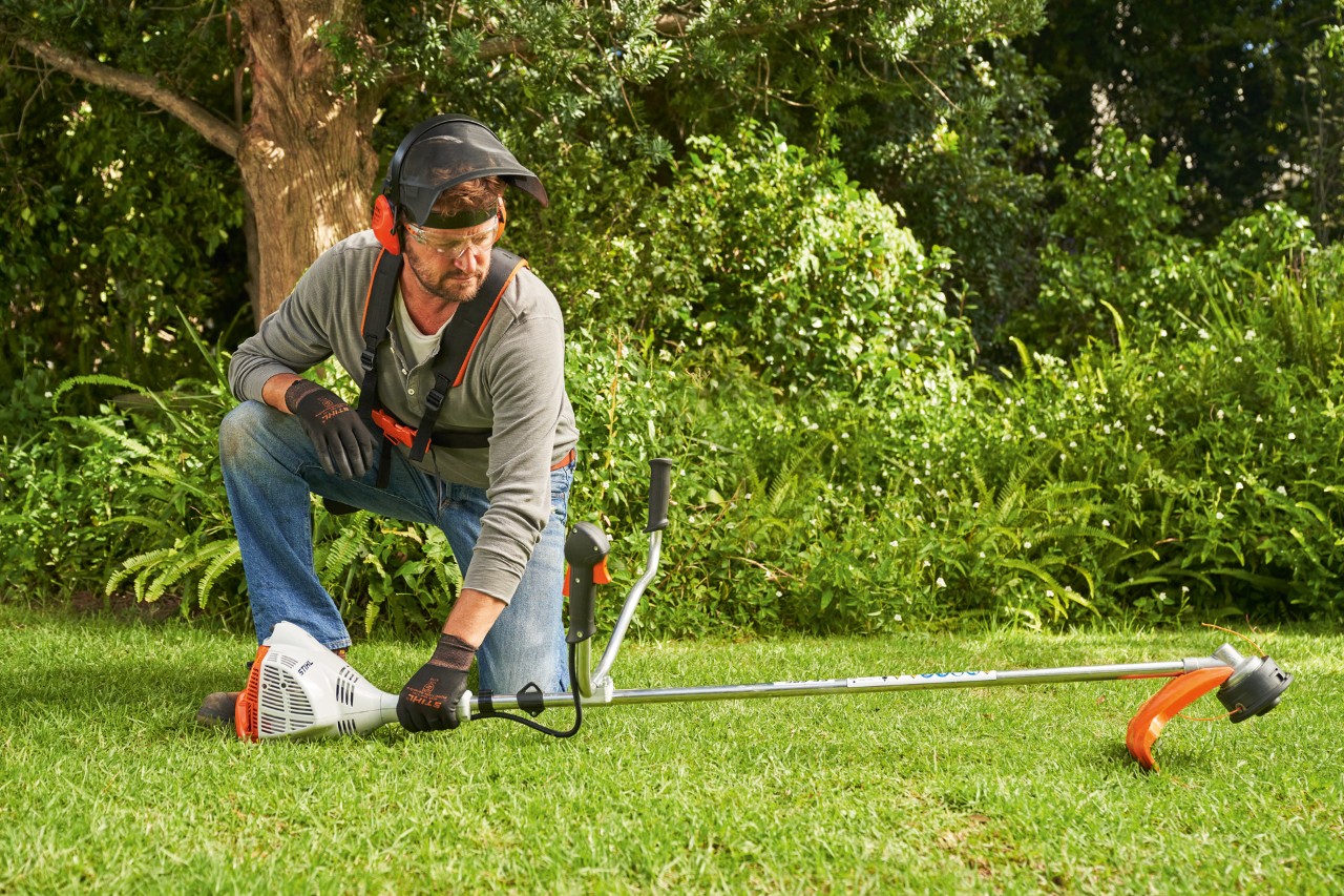 Egy férfi az indításhoz a földre helyezi a STIHL FS 56 benzinmotoros kaszát
