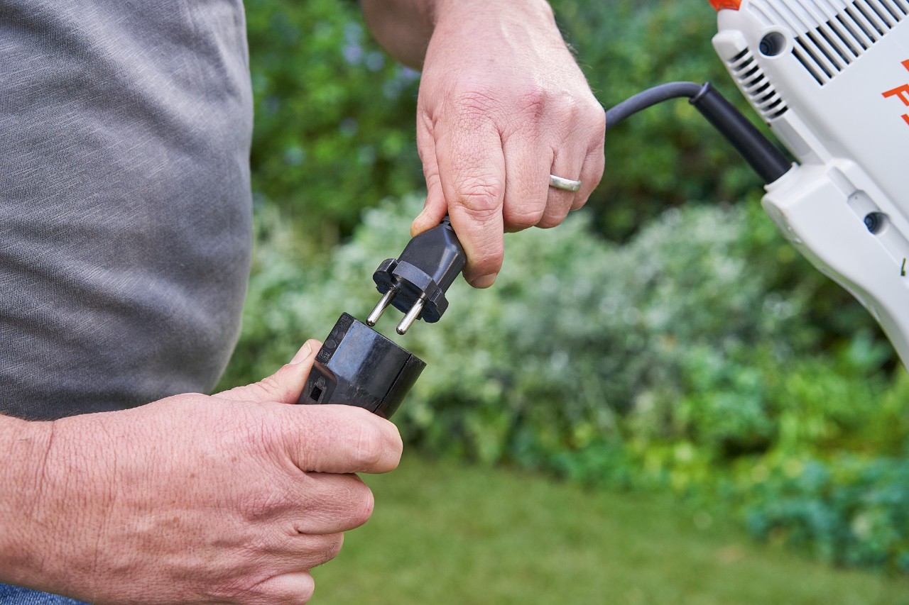 Védőkesztyűt viselő férfi megnyomja az elektromos szegélynyíró kapcsolóemeltyűjét a STIHL FSE 60 beindításhoz