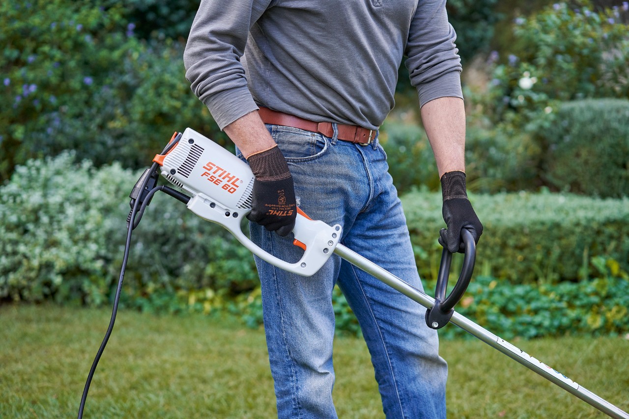 Védőkesztyűt viselő férfi két kézzel tartja a STIHL FSE 60 elektromos szegélynyírót