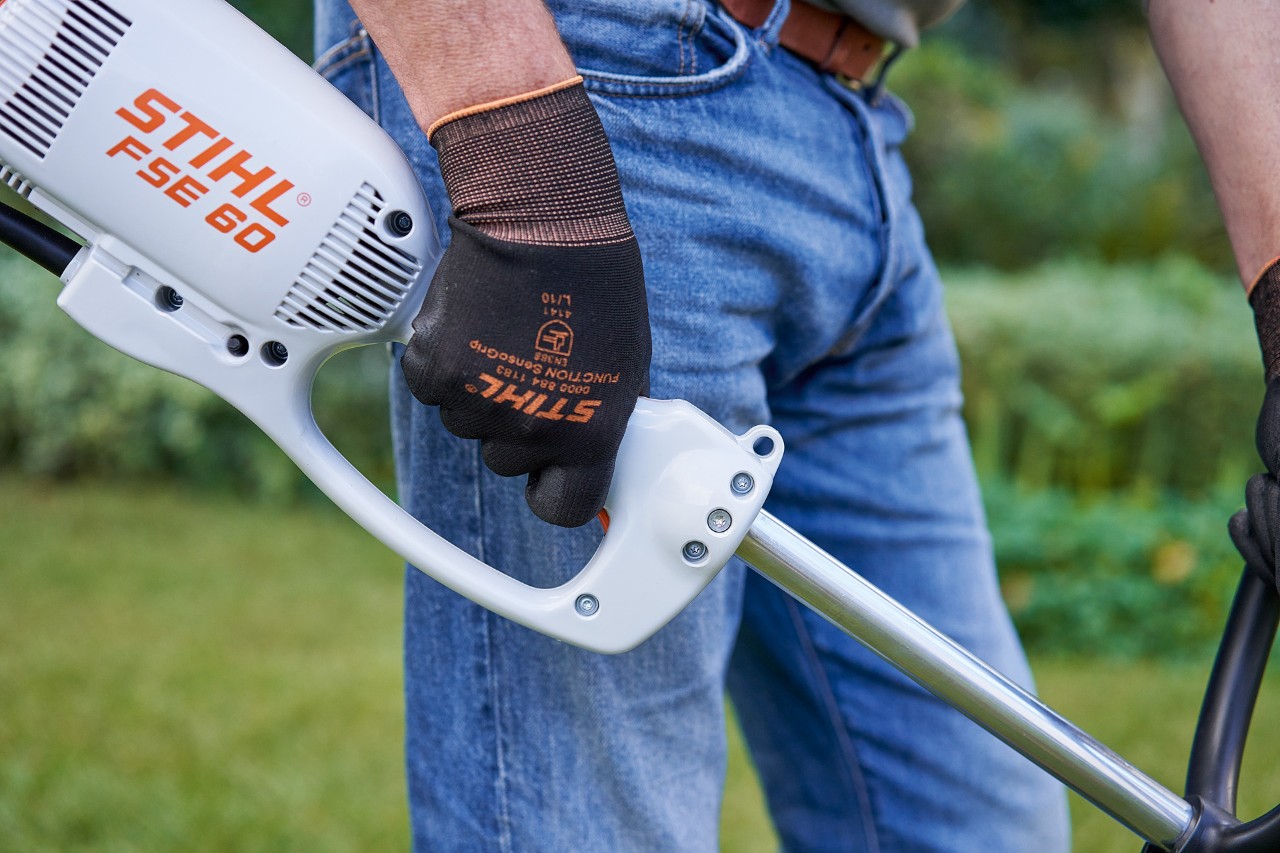 Egy férfi megnyomja a STIHL FSE 60 elektromos szegélynyíró kezelőfogantyúján lévő kapcsolót