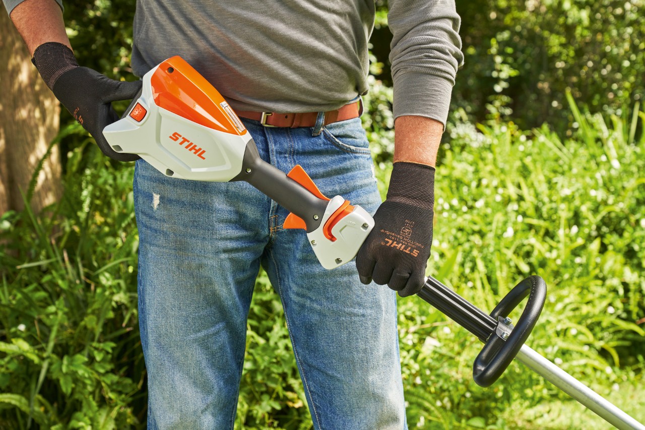 Egy férfi védőkesztyűvel ellenőrzi az akkumulátoros kasza akkumulátorát a STIHL FSA 60 motoros kasza indításához