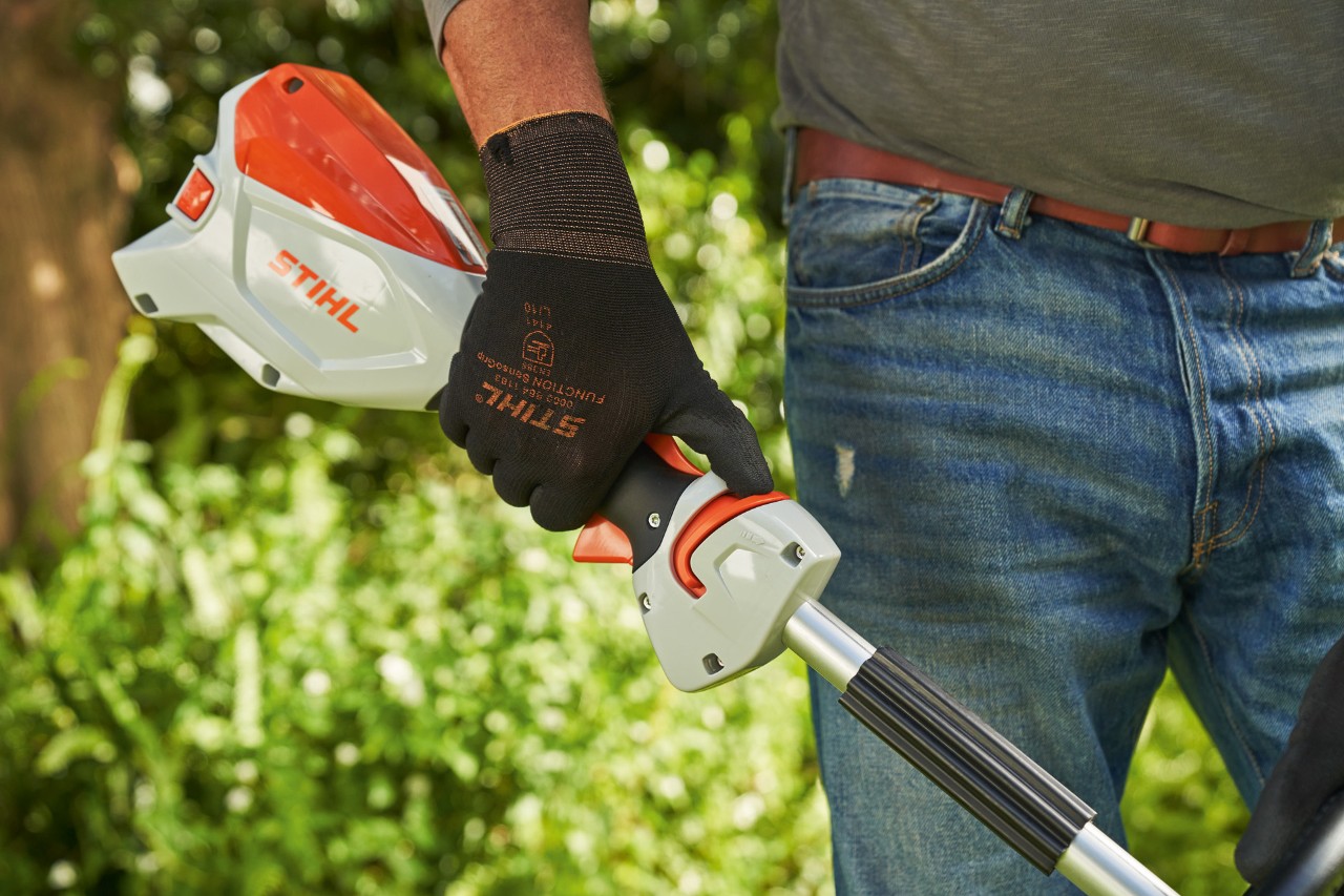 Védőkesztyűt viselő férfi az STIHL FSA 60 akkumulátoros kasza reteszkioldóját a körfogantyú felé tolja.