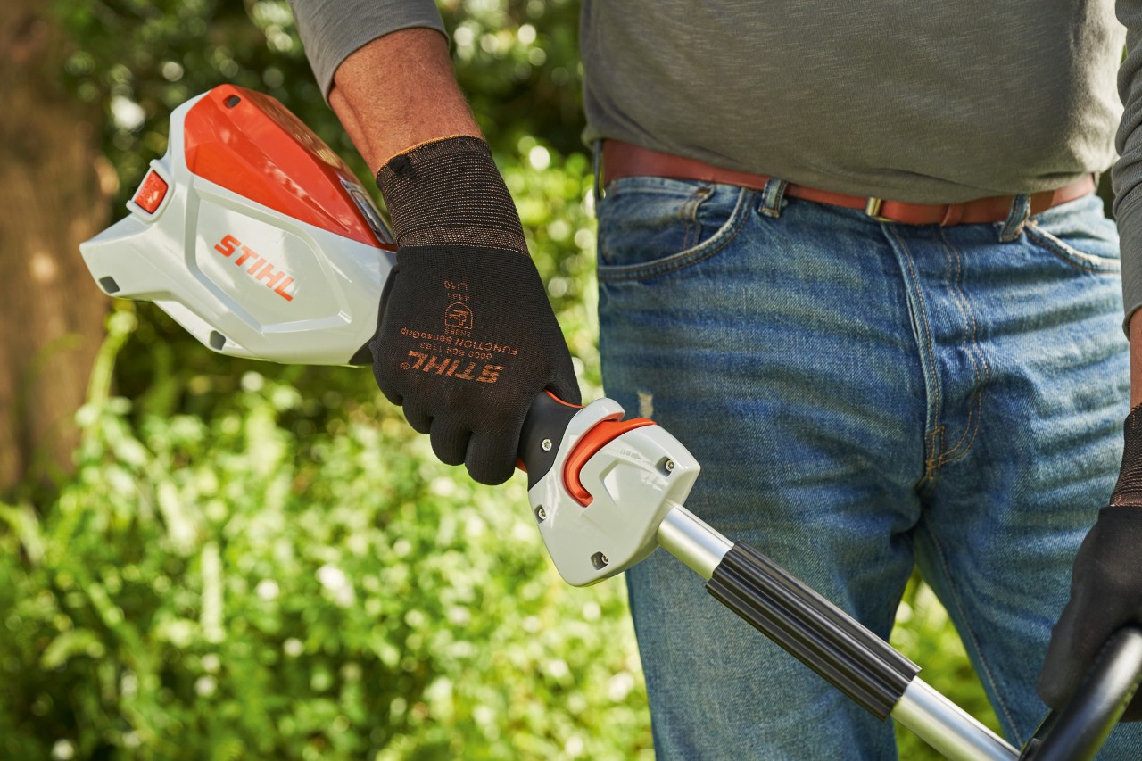 Védőkesztyűt viselő férfi megnyomja az akkumulátoros kasza kapcsolóemeltyűjét a STIHL FSA 60 beindításhoz
