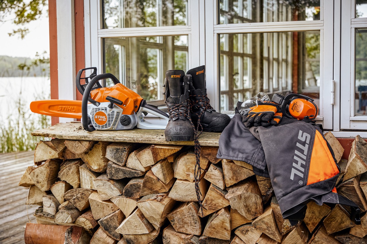 A STIHL védőruházat és az MS 162 motorfűrész a polcon a tűzifa fölött