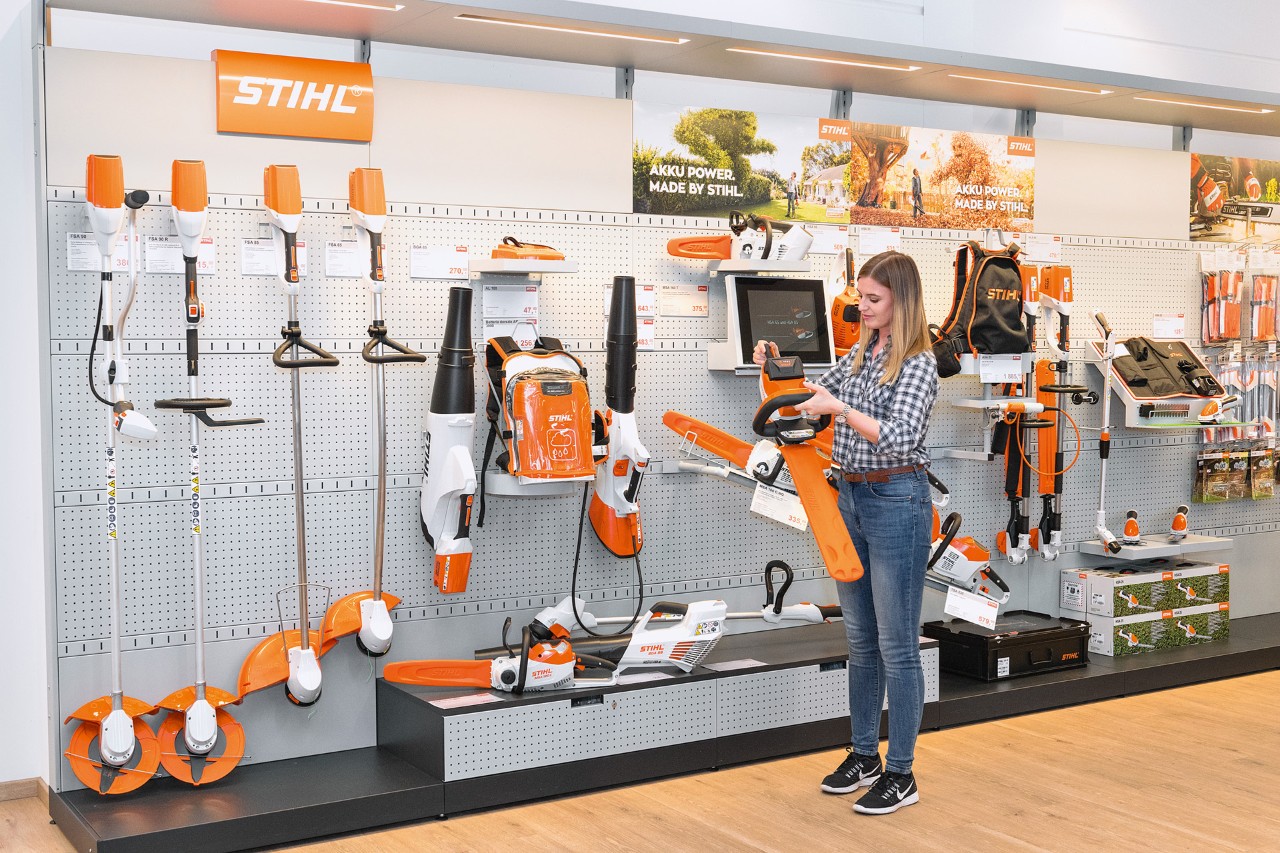 Egy STIHL szakkereskedőnél egy fiatal nő egy polc előtt STIHL láncfűrészt szeretne ingyenesen tesztelni