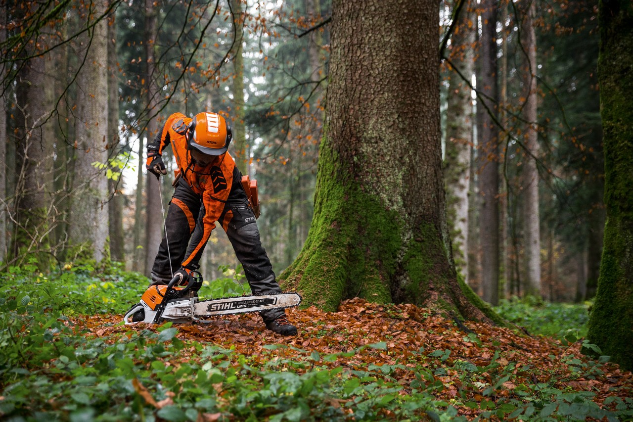 Védőruházatban dolgozó férfi MS 500i STIHL benzines motorfűrészt indít be a földön az erdőben
