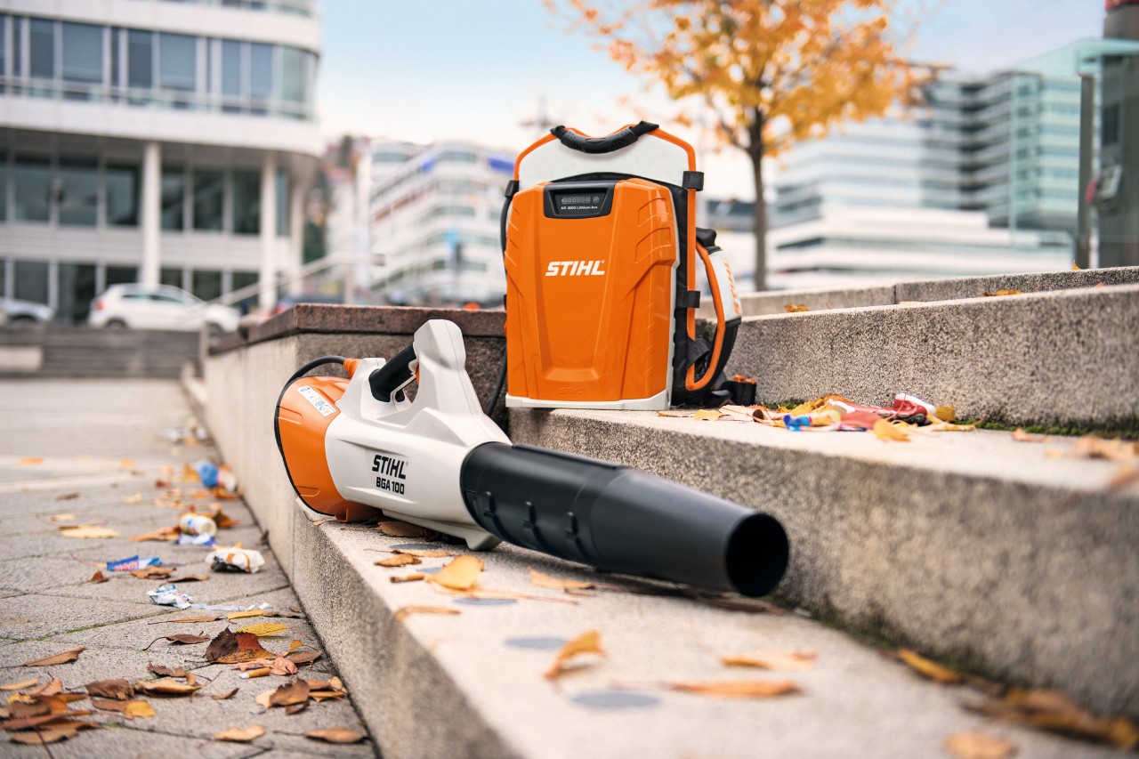 Egy kőlépcsőn lehullott falevelek mellett egy STIHL BGA 100 akkus lombfúvó és a háton hordozható profi STIHL AR 3000 L akkumulátor látható