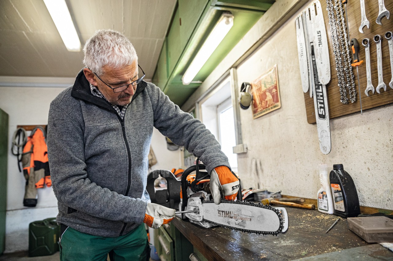 Egy férfi egy műhelyben egy STIHL Rollomatic E vezetőlemezes motoros fűrészen csavarozást végez 