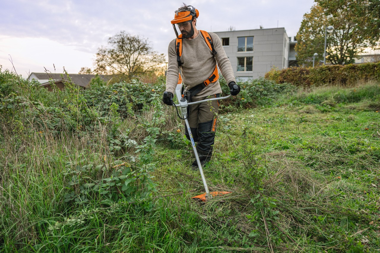 Egy férfi STIHL védőfelszerelésben STIHL FSA 200 akkumulátoros fűkaszával gazzal benőtt zöld területet nyír