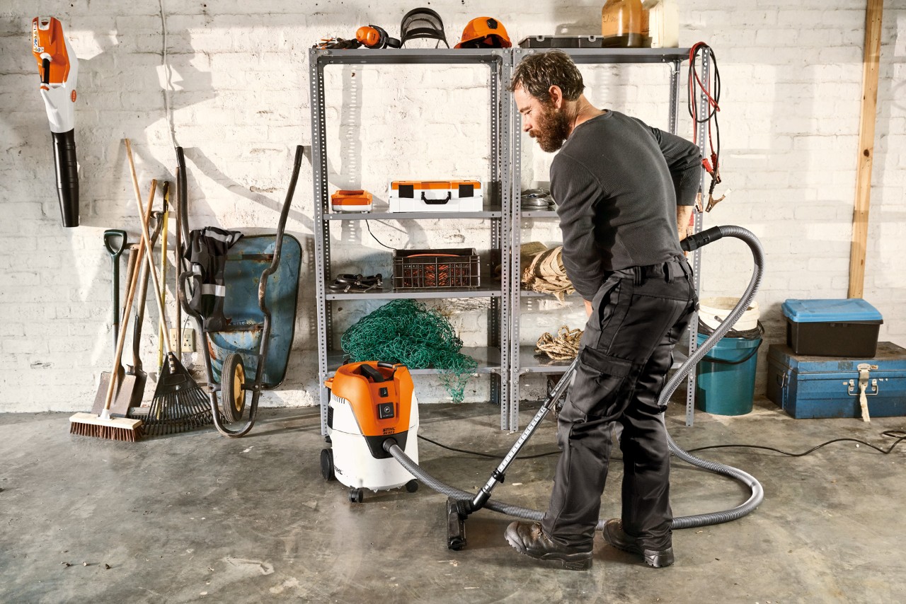 Egy férfi STIHL SE 62 E száraz-nedves porszívóval porszívózza a garázs padlóját