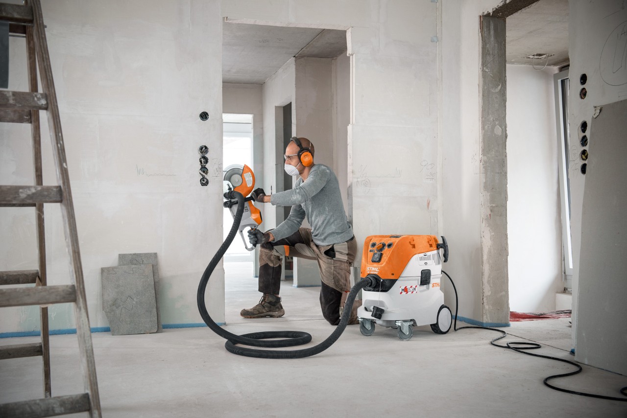 Egy férfi STIHL SE 133 ME száraz-nedves porszívót használ a STIHL TSA 230 vágótárcsás géppel végzett munkánál