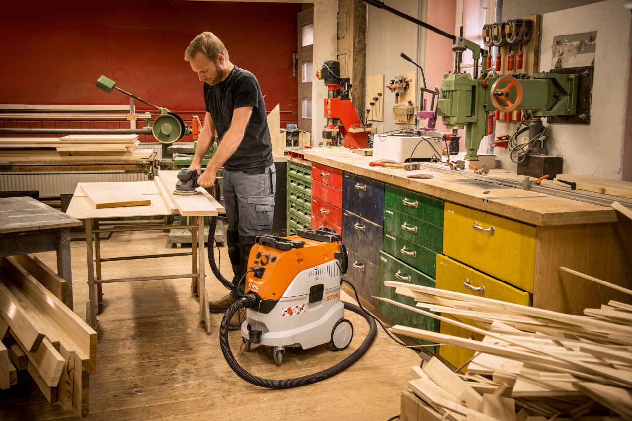 Egy férfi STIHL SE 133 ME száraz-nedves porszívót használ egy műhelyben falécekkel végzett munka során
