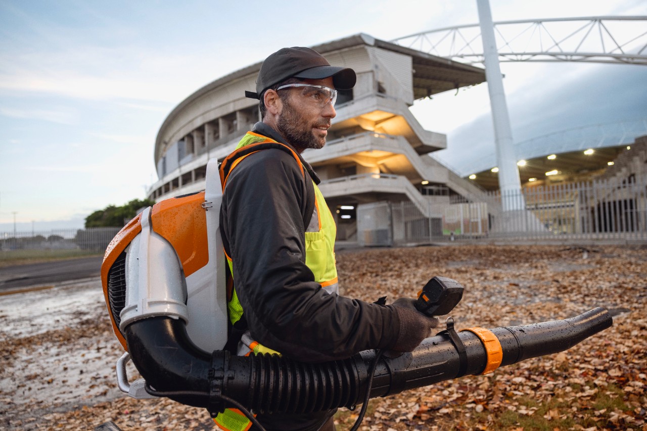 Késő este valaki az ALLPRO STIHL BRA 600 akkumulátoros levélfúvóval takarítja el a leveleket és a hulladékot egy stadionból.