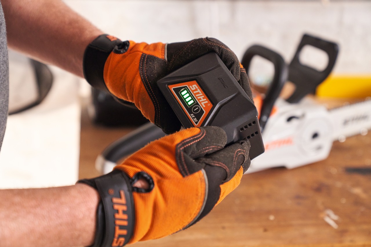 STIHL védőkesztyűt viselő ember a kezében tartja a STIHL lítium-ion akkumulátort