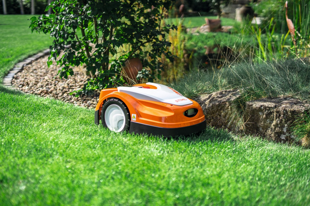 A STIHL iMOW RMI 422 egy kerti gyepen egy kis kőfal mentén nyír.