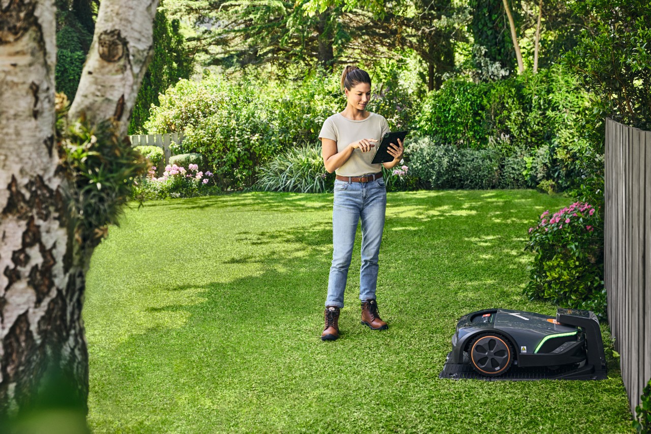 Egy nő a STIHL iMOW® EVO-t táblagépről irányítja a kertjében
